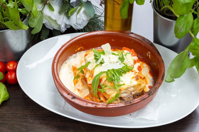 A rustic ceramic bowl of creamy soup topped with melted cheese and green onions, served on a white plate surrounded by fresh herbs
