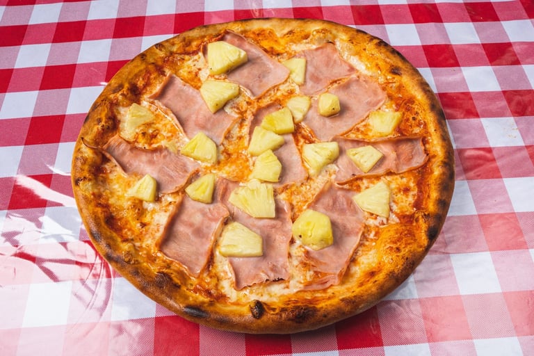 Pizza with ham and pineapple on red and white checkered tablecloth