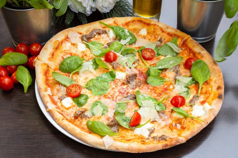 Freshly baked pizza topped with ham, mozzarella, red tomatoes, and fresh basil leaves on a white plate