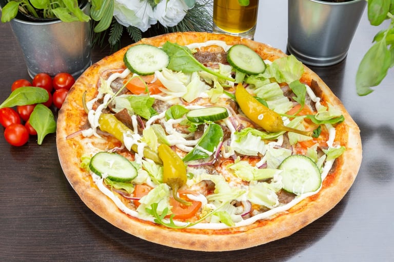 Vegetarian pizza topped with cucumbers, peppers, onions, and fresh greens on a dark table with potted plants